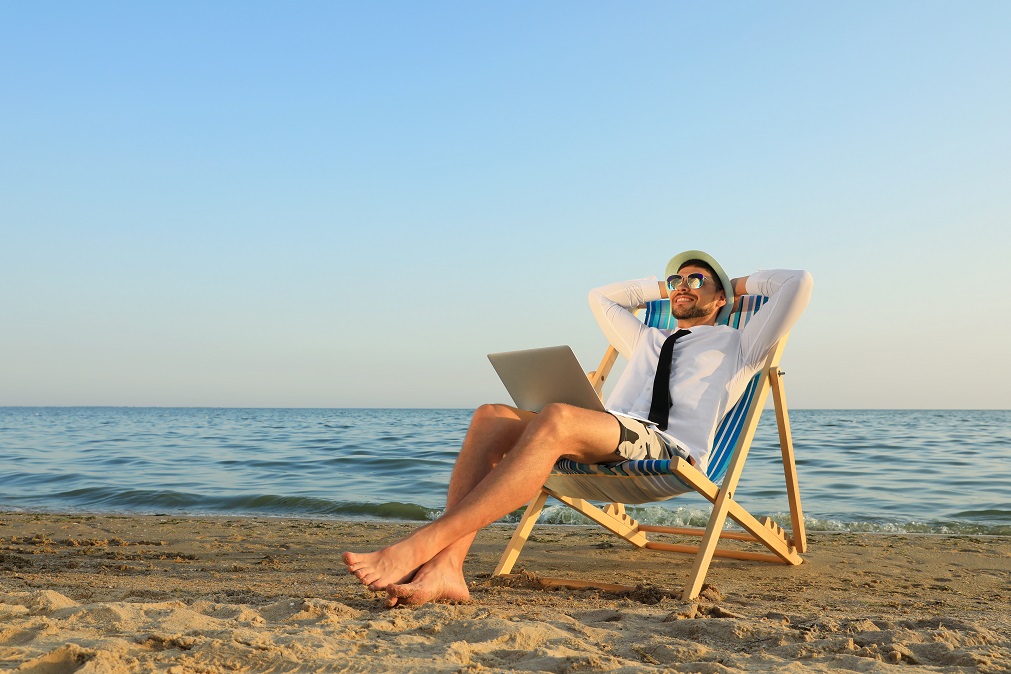 Mann im Hemd entspannt mit Laptop auf Liegestuhl am Strand