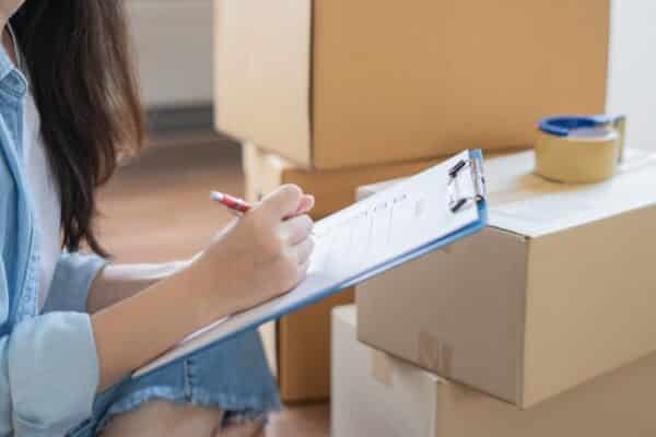 Rufnummernmitnahme: Umzug von Rufnummern - Frau mit Checkliste vor gepackten Kartons